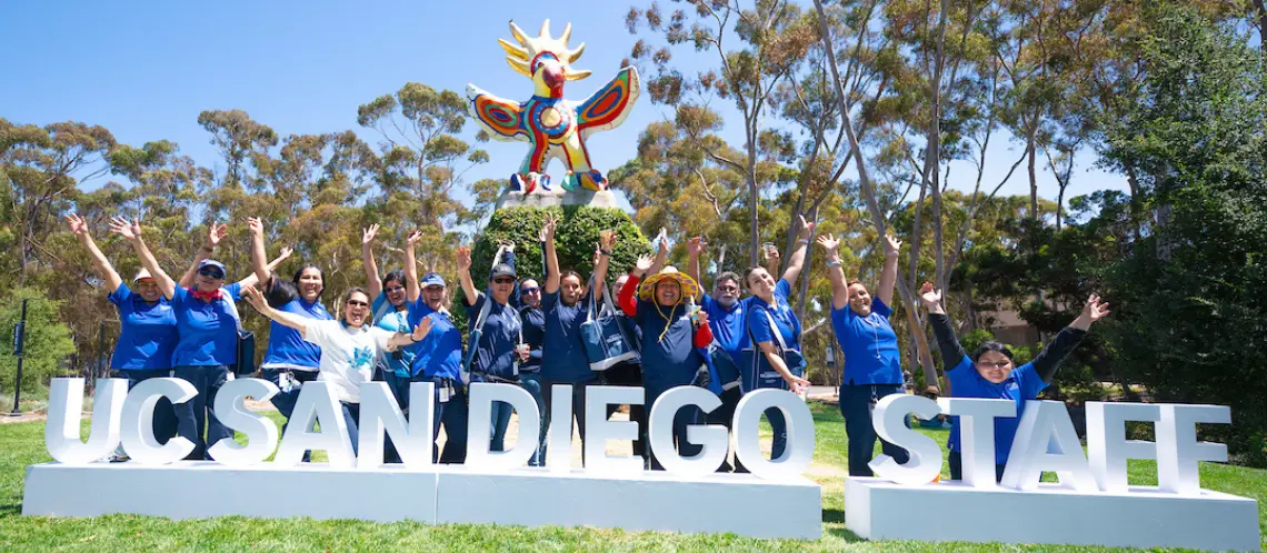 Staff standing infront of a sign that says "UC San Diego Staff" on Sun God Lawn. 